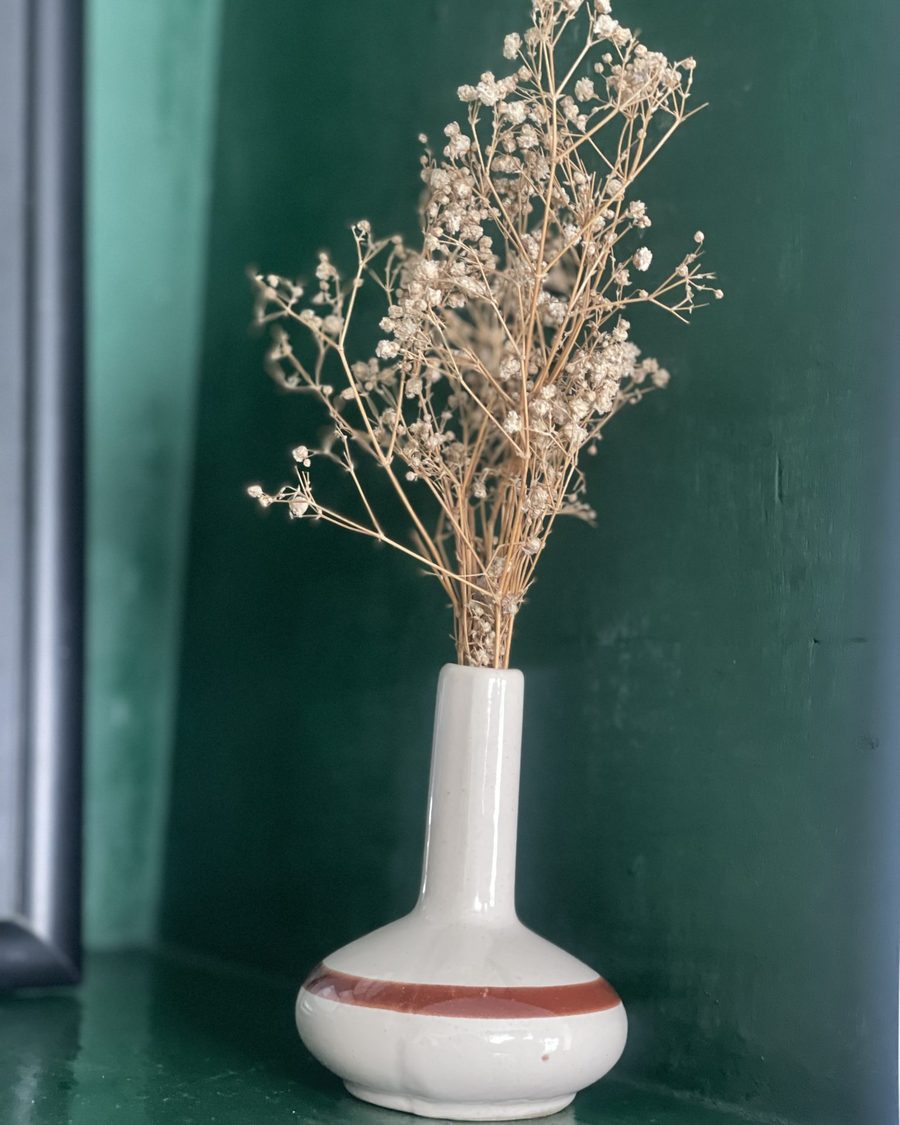 Flores secas en un jarrón de cerámica sobre un fondo verde oscuro, transmitiendo calma y calidez